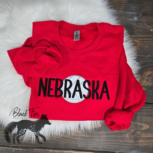 Red sweatshirt with 'NEBRASKA' printed on it, lying on a wooden surface.