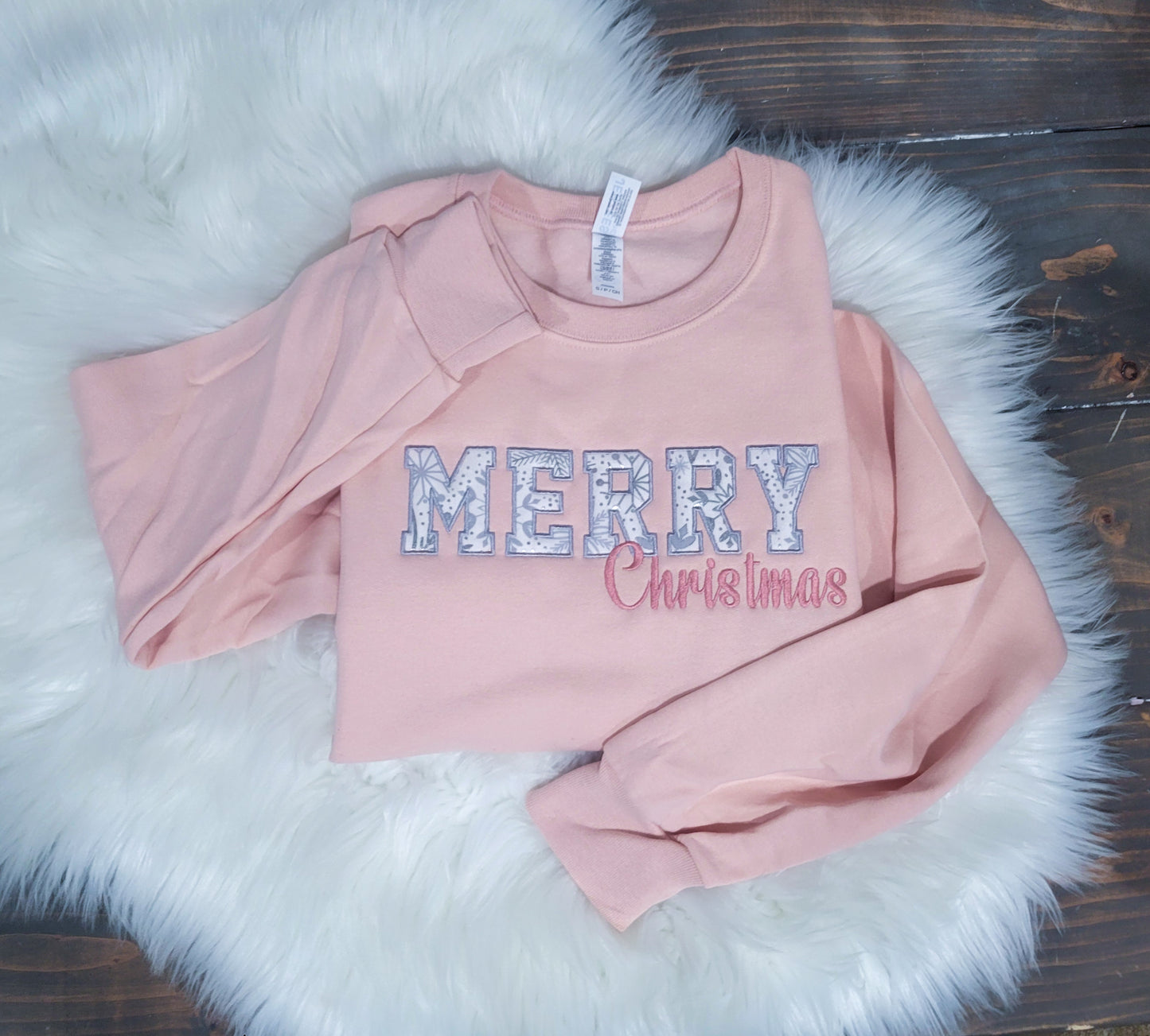 A pink crewneck sweatshirt with 'Merry' with foil snowflake fabric appliqued behind it then Christmas in cursive right underneath.