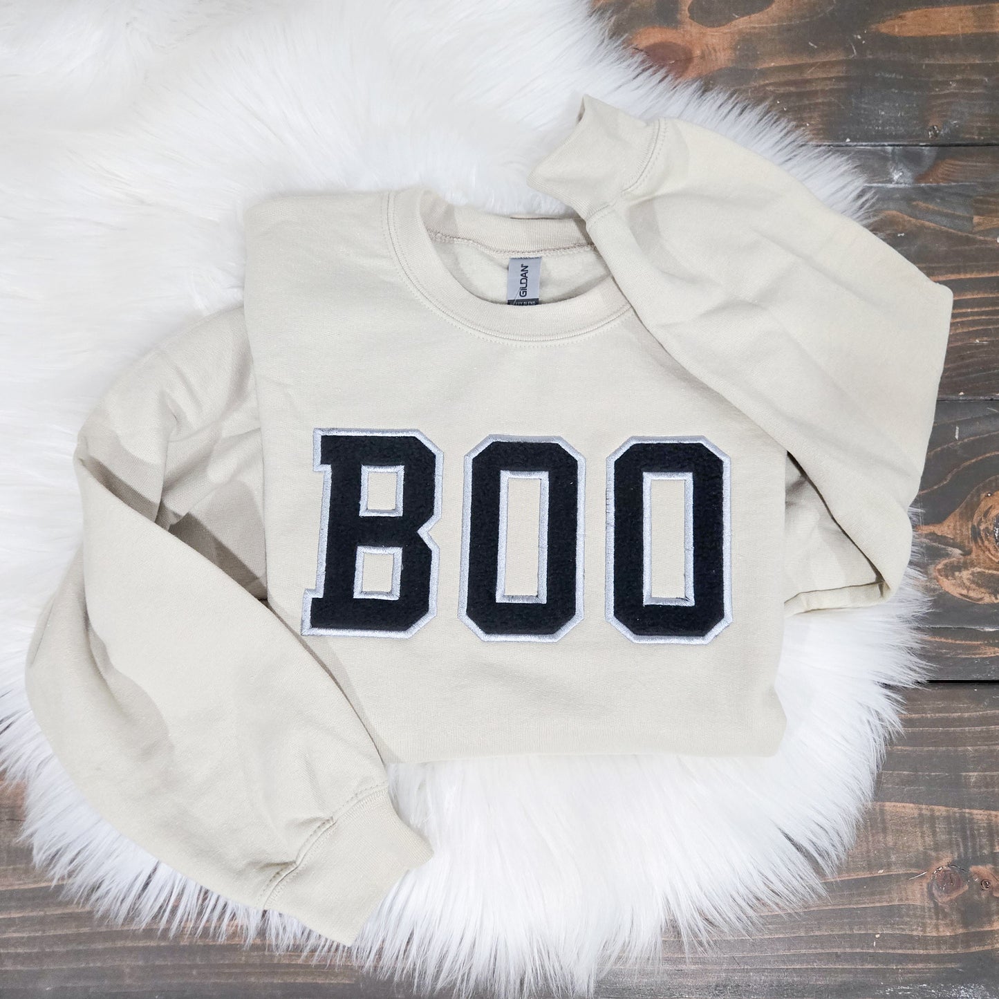 Beige sweatshirt with 'BOO' patch on a wooden surface