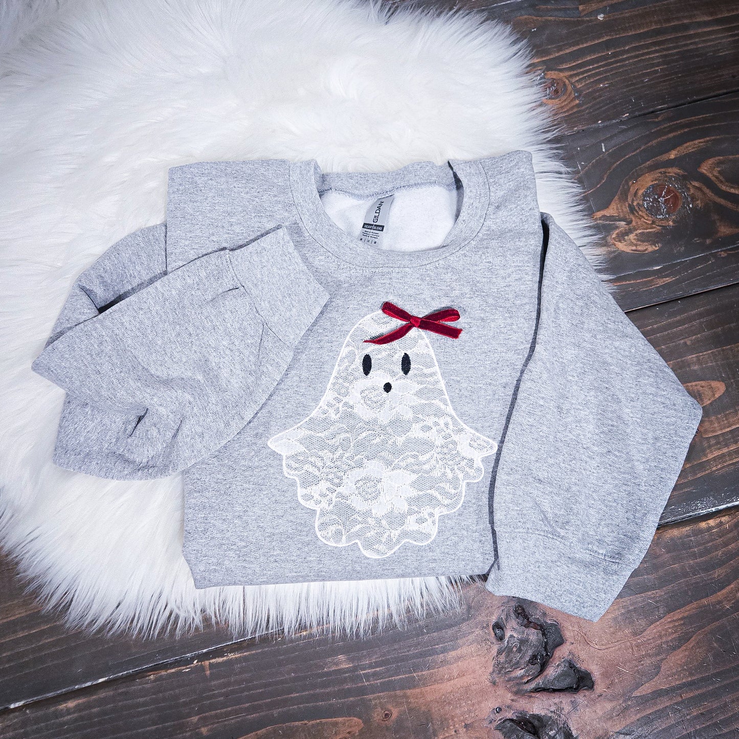 Gray sweatshirt with a ghost design and red bow on a wooden surface