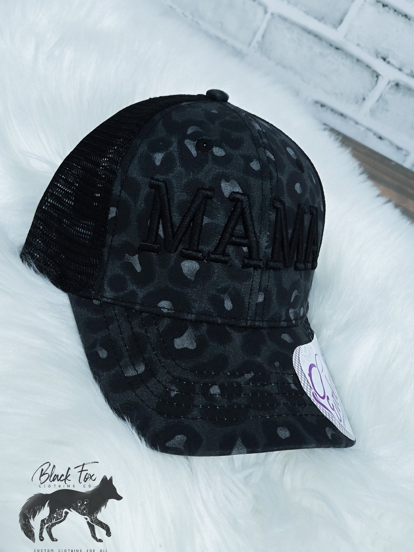 A black trucker hat with a brown leopard print and the text 'MAMA' embroidered in capital letters on the front.