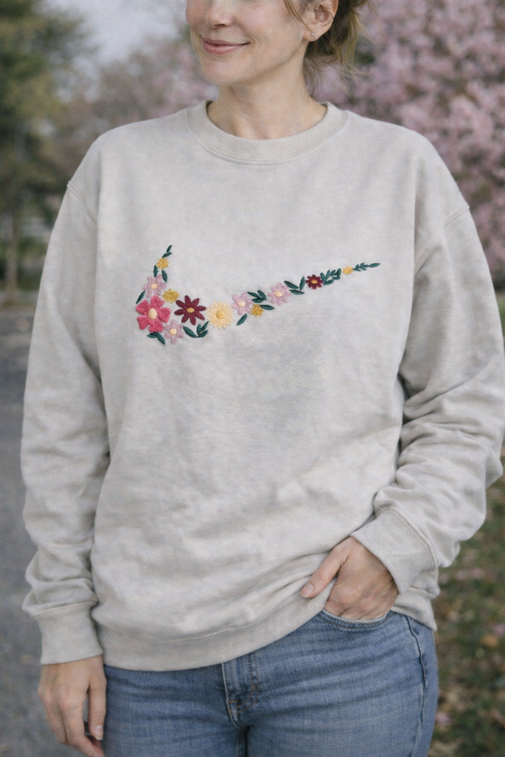 Person wearing a light tan sweatshirt with a floral Nike logo design outdoors.