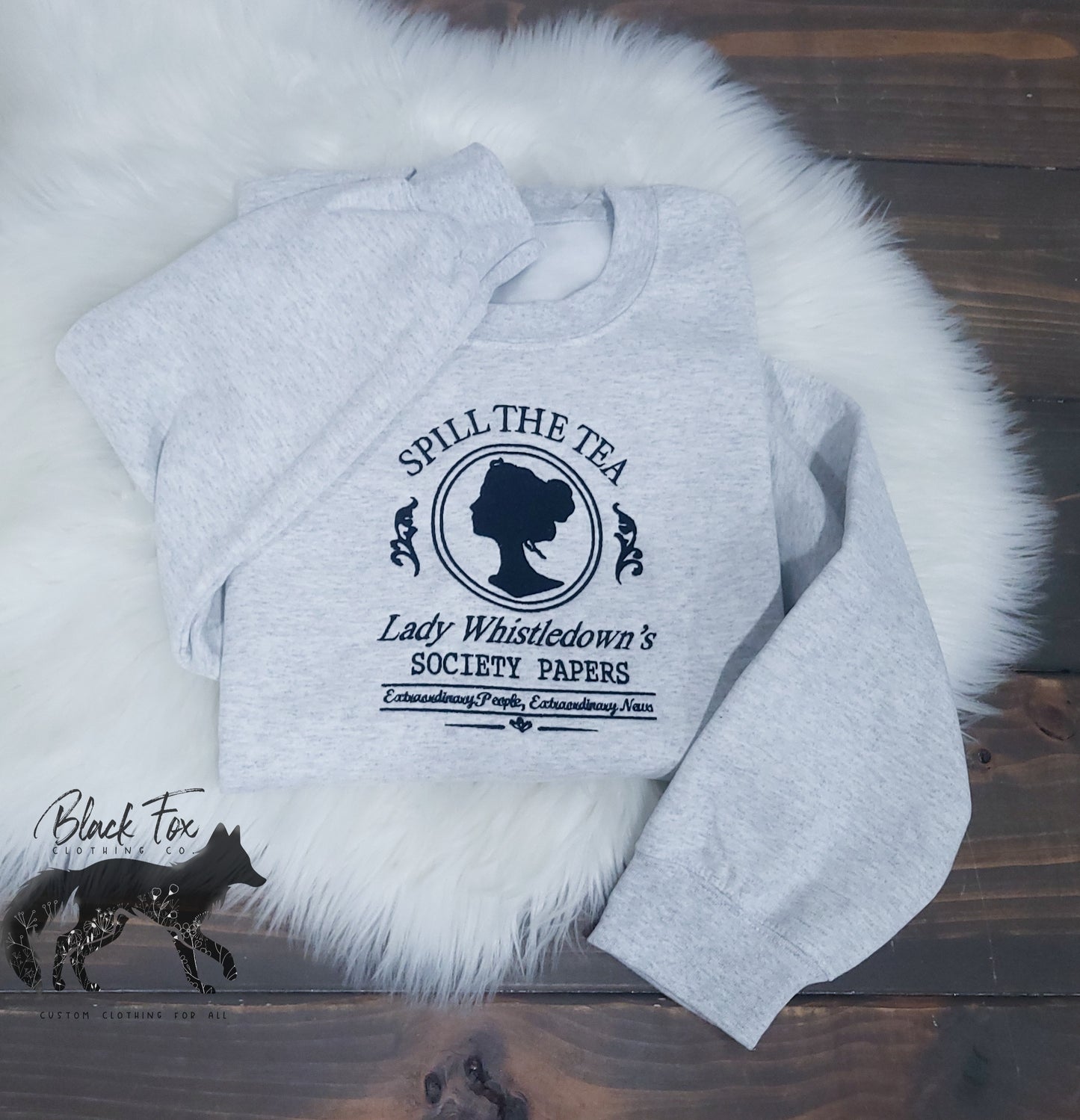 Gray sweatshirt with 'Spill the Tea' design on a wooden surface with fur.