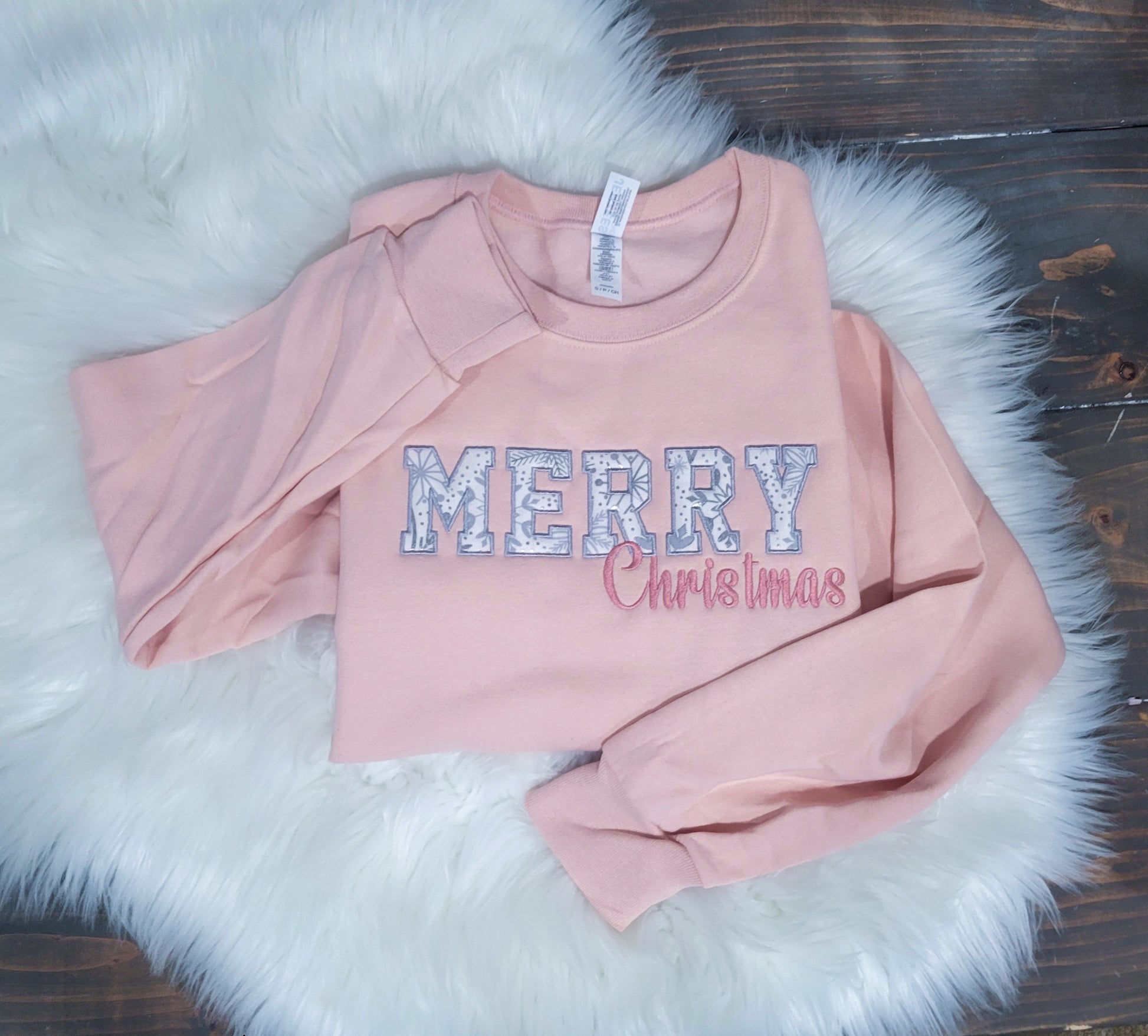A pink crewneck sweatshirt with 'Merry' with foil snowflake fabric appliqued behind it then Christmas in cursive right underneath.