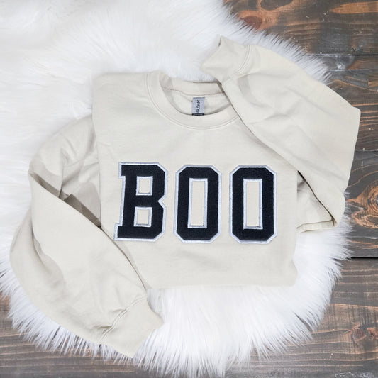 Beige sweatshirt with 'BOO' patch on a wooden surface