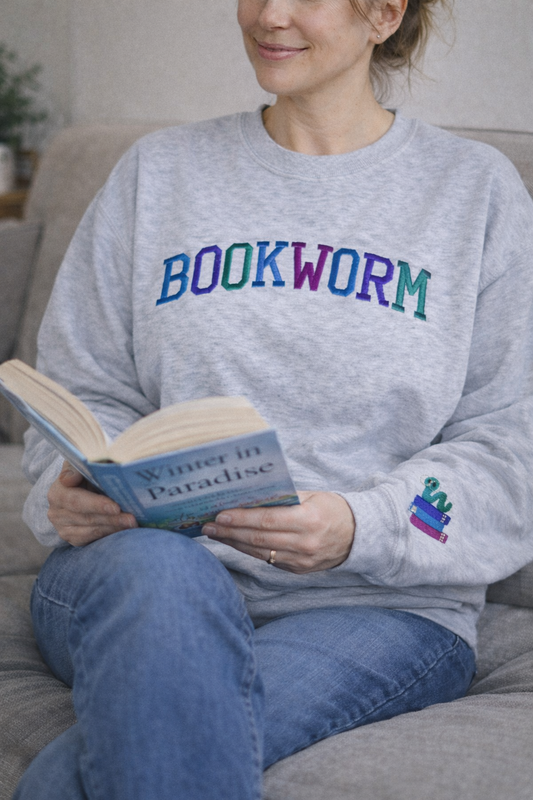 Person wearing a gray sweatshirt with 'BOOKWORM' in colorful letters, holding a book.