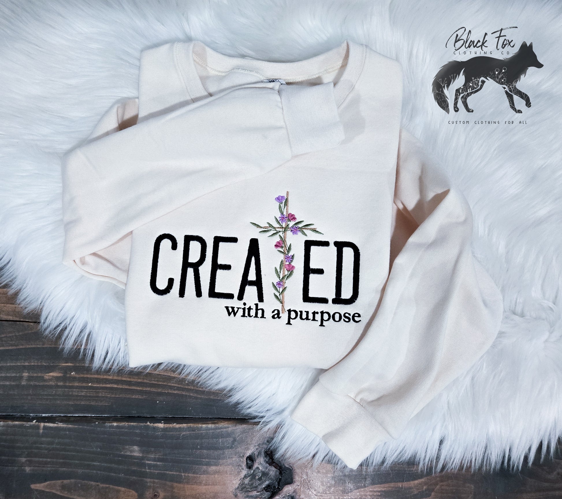 A beige Gildan fleece crewneck sweatshirt with the text 'CREATED with a purpose' on the front, displayed on a white fluffy surface.