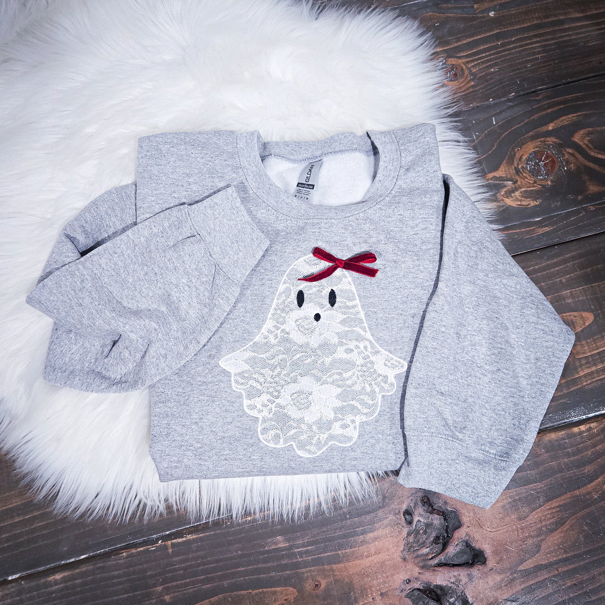 Gray sweatshirt with a ghost design and red bow on a wooden surface