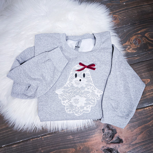 Gray sweatshirt with a ghost design and red bow on a wooden surface