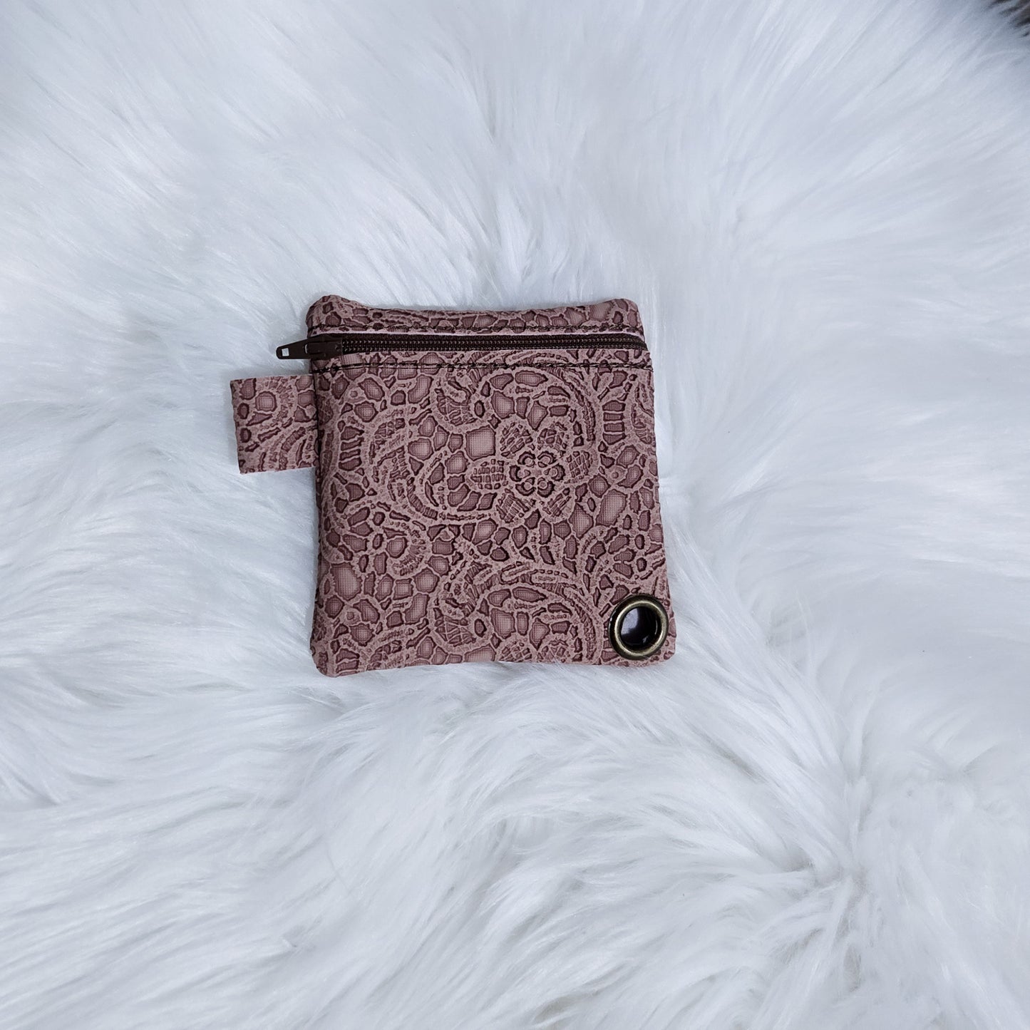 Pink lace-patterned pouch on a white fluffy surface