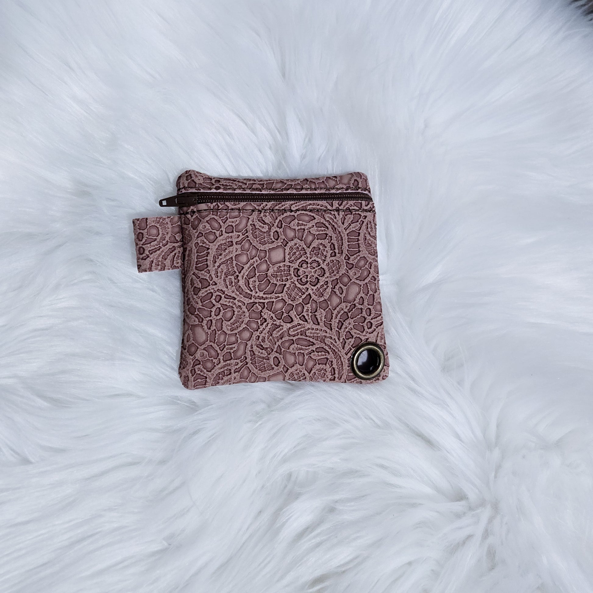 Pink lace-patterned pouch on a white fluffy surface