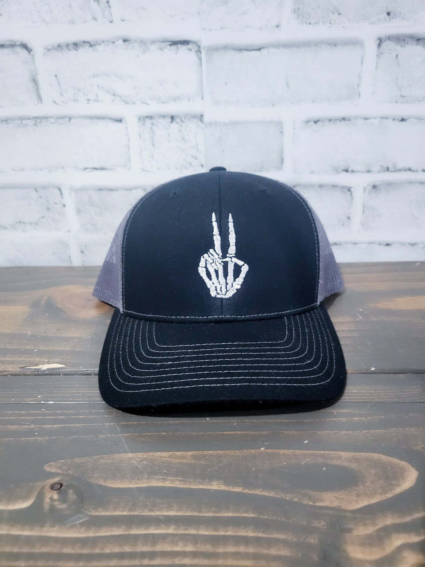 Black trucker hat with a grey skull and peace sign embroidery on the front.