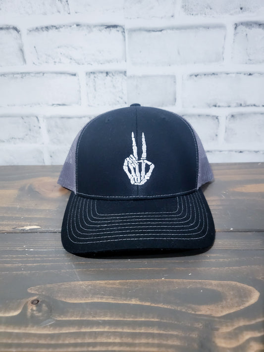 Black trucker hat with a grey skull and peace sign embroidery on the front.
